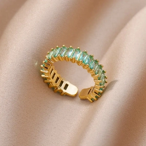 Detail of adjustable gold ring with baguette-cut light green stones on satin fabric