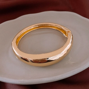 Detail of a polished gold-tone wide cuff bracelet with a hinge clasp on a ceramic tray