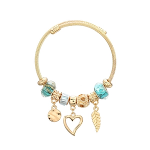 Bracciale a cavo dorato con perline turchesi e ciondoli a foglia e cuore su sfondo bianco