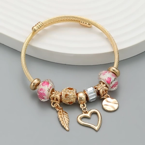 Dettaglio di un bracciale a spirale dorato con perline floreali e ciondoli a cuore e foglia