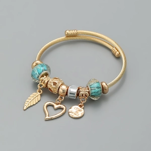 Dettaglio di un bracciale a corda dorato con ciondoli a foglia, cuore e targa LOVE & PEACE