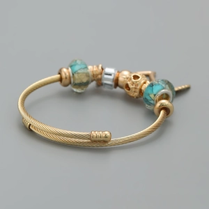 Dettaglio del bracciale ritorto dorato con perline marmorizzate e ciondolo a cuore