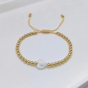 Minimalist gold beaded bracelet featuring a white heart shell pendant and adjustable cord