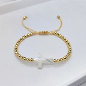 Minimalist gold beaded bracelet with a white shell cross pendant and adjustable cord