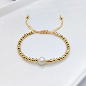Close-up of gold beaded bracelet featuring a white shell pearl and adjustable cord