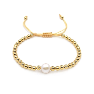 Detail of beaded gold bracelet with a central white pearl and adjustable woven cord