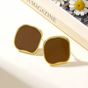 Detail of square brown enamel stud earrings with gold metal frame on a beige background
