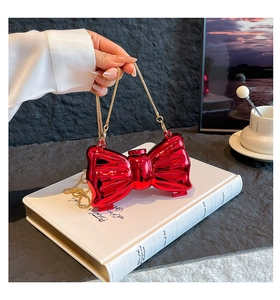 Macro detail of red metallic bow clutch bag with gold chain strap on white book