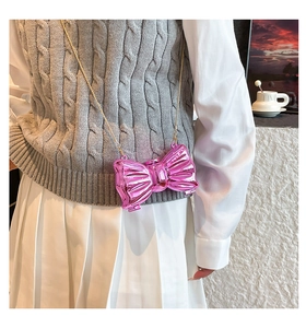 Mirror pink bow-shaped mini bag with gold chain strap worn by a model