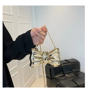 Close-up of golden bow-shaped evening clutch bag with glossy metallic finish and chain strap