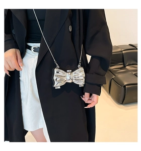 Detail of silver metallic bow bag with chain strap shown on a black leather background