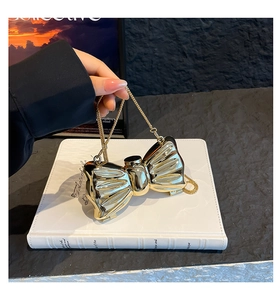 Close-up of golden bow-shaped evening bag with metallic mirror finish and chain