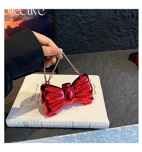 Detail of red bow-shaped metal mini bag with gold chain and mirrored finish