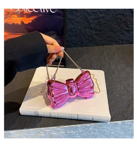Detail of pink metallic bow-shaped evening bag with gold chain strap on white book