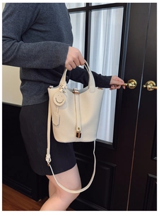 Detail of creamy white pebble leather bucket bag with gold lock and smiling charm pendant