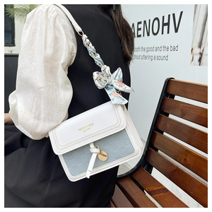 Detail of blue textured crossbody bag with white flap and decorative silk scarf bow