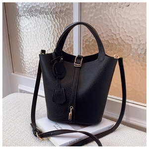 Detailed close-up of black lychee leather bucket bag with gold lock on white books