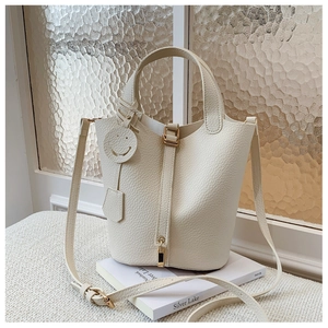 Detail of cream lychee leather bucket bag with gold hardware and smiley face charm