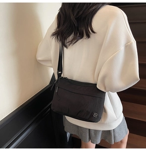 Detail of a black nylon crossbody bag with a silver clover logo and adjustable wide strap