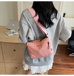 Detalle de un bolso bandolera de nailon rosa con correa ancha en una modelo femenina