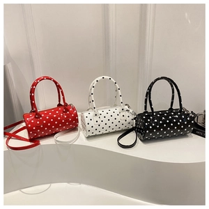 Three glossy polka dot cylinder handbags in red, white, and black on a white stand