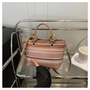 Close-up of woven straw bucket bag showing gradient stripes and brown leather knotted handle