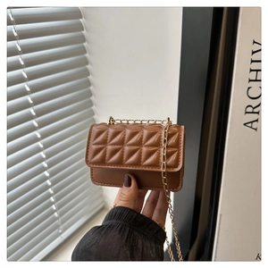 Detailed view of mini brown quilted crossbody bag with gold chain strap held by hand