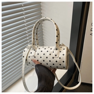 Detail view of white cylinder bag with black polka dots and detachable shoulder strap