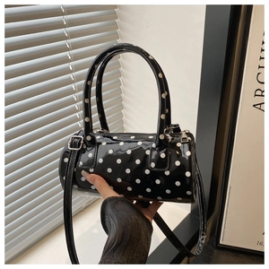 Close-up of polka dot cylinder bag featuring glossy patent leather and dual handles