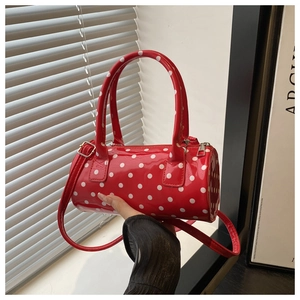 Detailed view of red polka dot barrel bag held by hand featuring glossy patent leather finish
