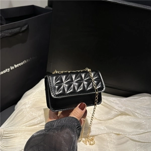Chic black quilted crossbody bag with gold chain strap held against a silk background