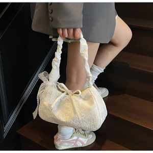 Detail of white lace tote bag with ruffled handles and organza bow on wooden stairs