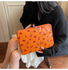 Gros plan de la pochette ordinateur orange à motifs cerises et double fermeture éclair