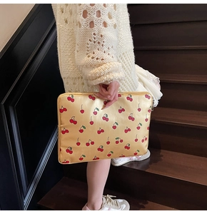 Détail d'une housse d'ordinateur en satin doré à motifs cerises tenue par un mannequin