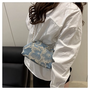 Detail of light blue embroidered floral chain bag worn over the shoulder by a model