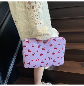 Close-up of purple laptop sleeve with red cherry pattern held against wood background
