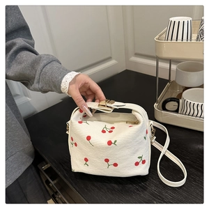 Close-up of white corduroy handbag with cherry prints and golden metal clasp detail