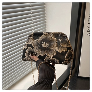 Close-up of golden floral embroidery on a black satin clutch bag with metal chain