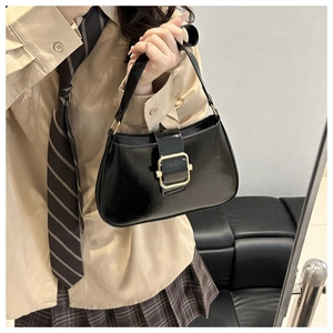 Detail of glossy black hobo bag featuring a large gold square buckle held by a model