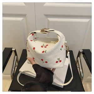 Detail of white knit crossbody bag featuring red cherry embroidery and gold clasp