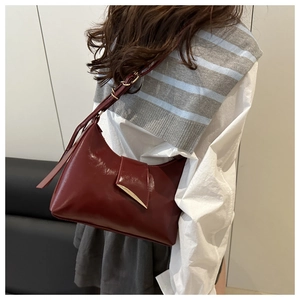 Detail of burgundy glossy leather underarm bag featuring a stylish gold V-shaped metal buckle