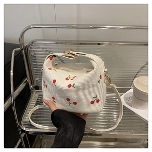 Close-up of white corduroy shoulder bag featuring red cherry embroidery and gold zipper