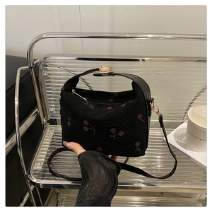Detail of black cherry pattern fabric handbag with golden hardware on a stylish shelf