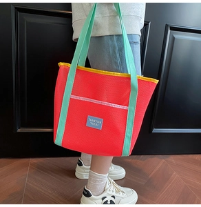 Detail of red mesh beach bag with mint green strap and yellow trim on wood background