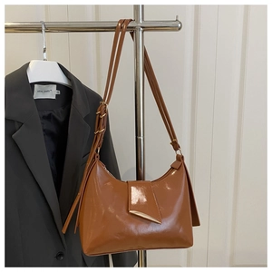 Detail of glossy caramel brown hobo bag featuring a metallic buckle and adjustable strap