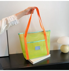 Detail of mesh tote bag with breathable texture and vibrant orange handles for beach use