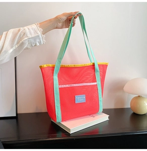 Detail of large mesh beach tote bag with orange net and mint green straps on a desk