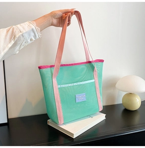 Close-up of green mesh tote bag featuring pink straps and a blue logo patch with internal pocket