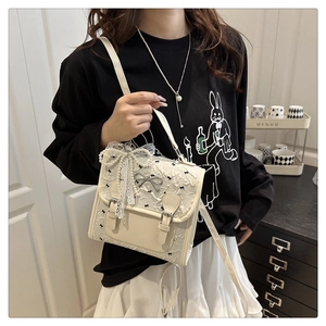 Detailed lace texture with black bow embroidery and pearl bow accent on a cream handbag