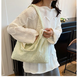 Gros plan d'une broderie florale vert clair sur un sac à bandoulière en toile souple